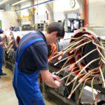 Industriearbeiter montieren elektrische Leitungen und prüfen Anschlüsse an einem großen Elektromotor in der Fertigungshalle